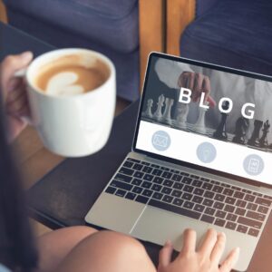 Photo of someone sitting at table, holding a mug of coffee and writing a blog